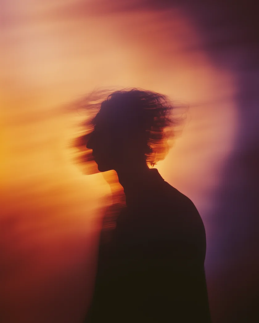 Silhouette of a person with blurred hair movement against a warm, orange and purple gradient background.